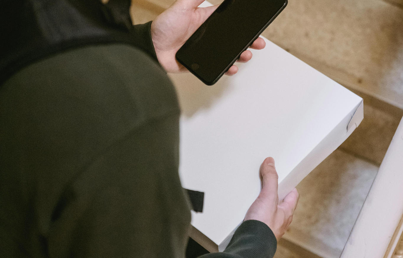 A delivery person checking their phone while holding a package on the stairs.